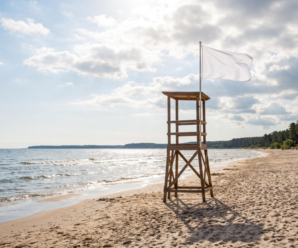 Drewniana wieża ratownika z białą flagą na pustej plaży w Rowach. O warunkach nad morzem przeczytasz w Eska Trójmiasto.
