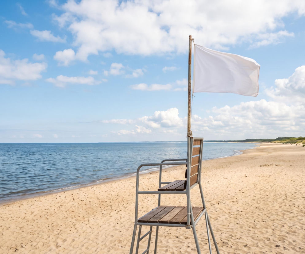 Biała flaga na maszcie przy wieży ratowniczej na pustej plaży. O pogodzie i kąpieli w Sarbinowie czytaj w SE Szczecin.
