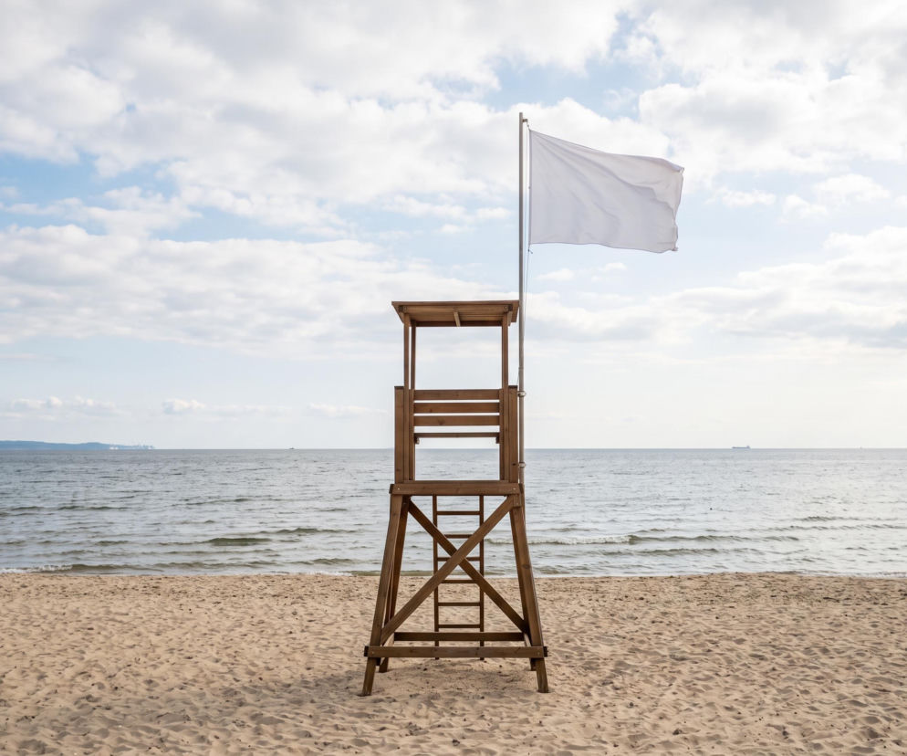 Drewniana wieża ratownicza na plaży z powiewającą białą flagą. O warunkach kąpieli w Sopocie przeczytasz na Eska Trójmiasto.