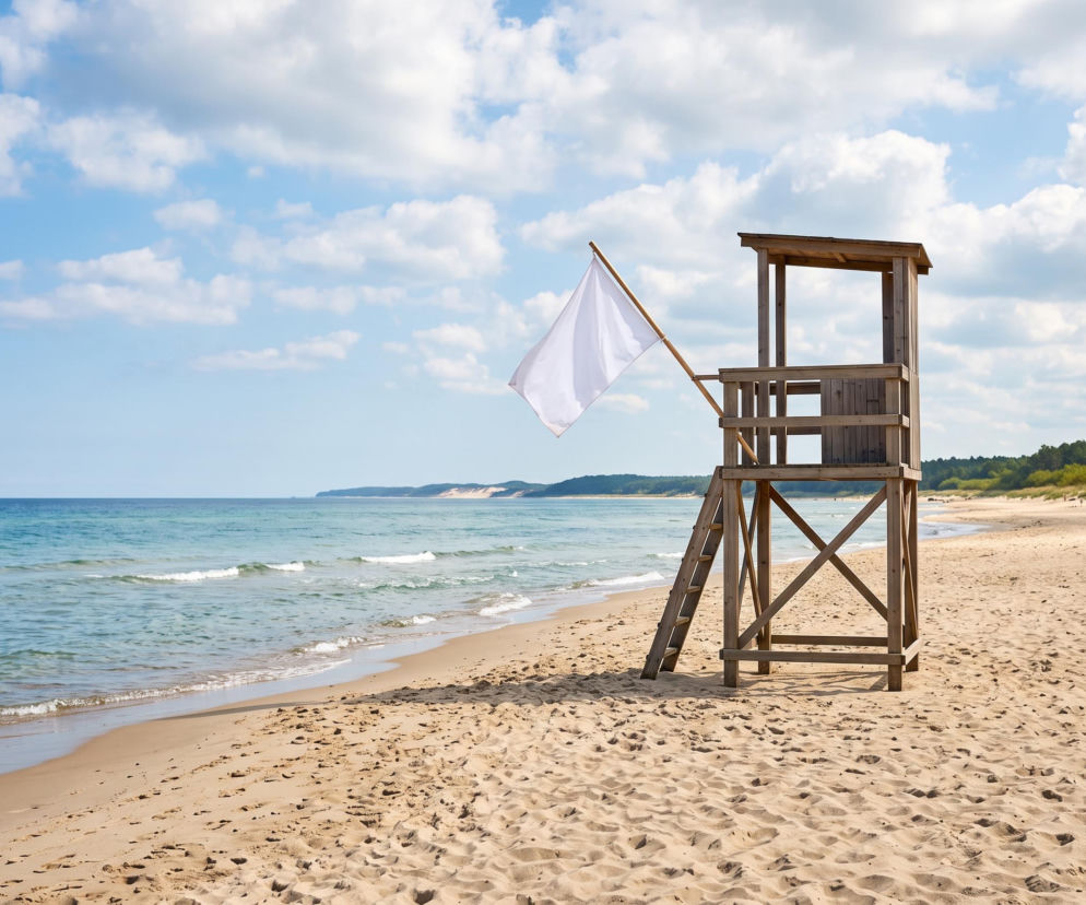 Drewniana wieża ratownika z białą flagą na pustej, piaszczystej plaży. O pogodzie w Stegnie pisze Eska Trójmiasto.