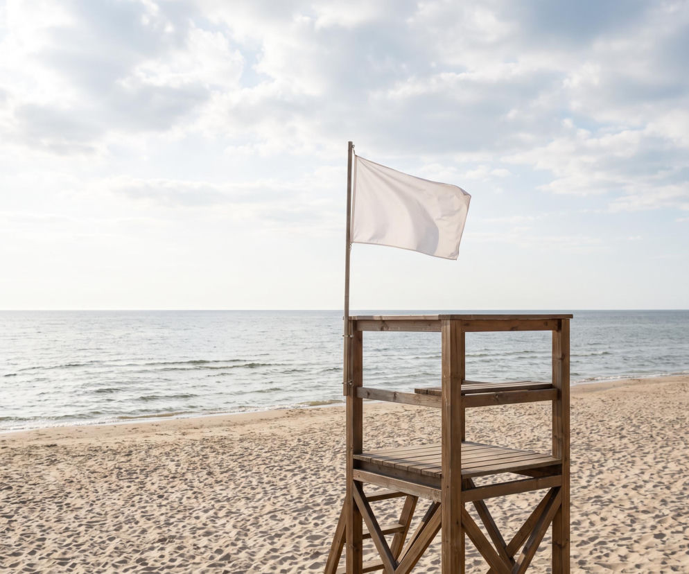 Biała flaga na drewnianej wieży ratowniczej na pustej plaży. O bezpieczeństwie w Świnoujściu przeczytasz na SE Szczecin.