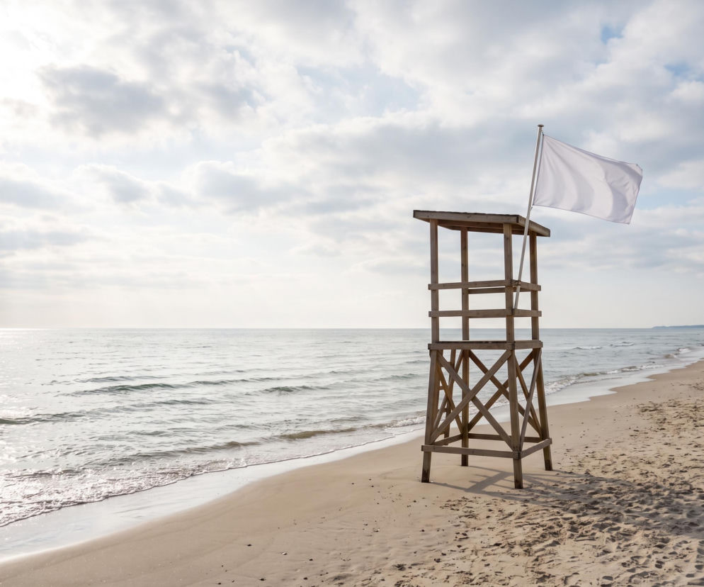 Drewniana wieża ratownika z białą flagą na piaszczystej plaży w Ustce. O warunkach nad morzem dowiesz się z Eska Trójmiasto.