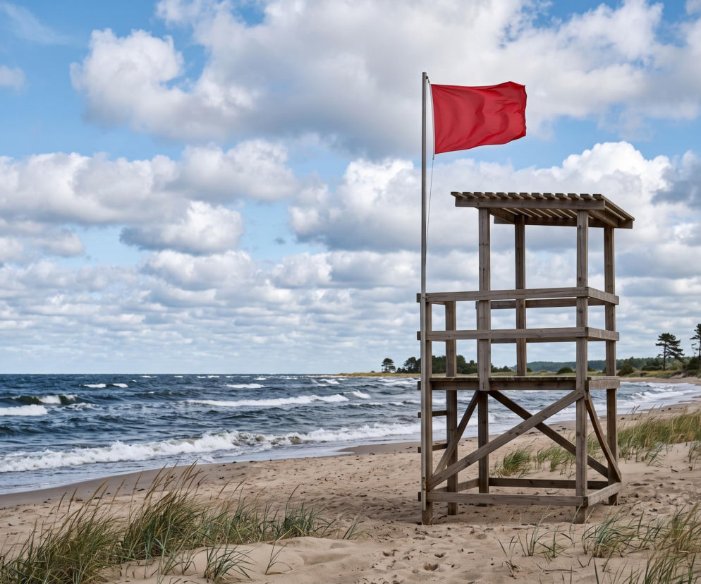 Czerwona flaga na wieży ratowniczej przy pustej plaży. O bezpieczeństwie w Ustroniu Morskim przeczytasz na SE Szczecin.