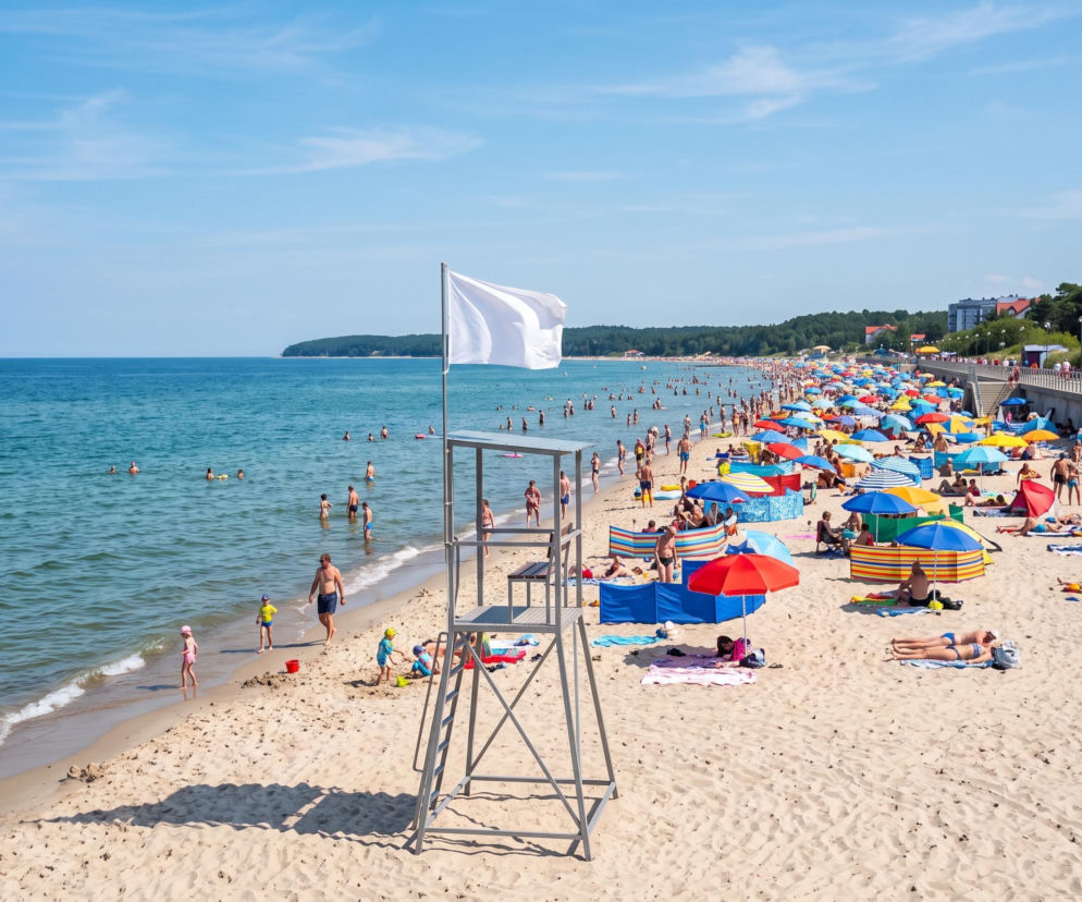 Słoneczna plaża w Ustroniu Morskim z białą flagą na wieży ratowniczej. O warunkach kąpieli przeczytasz na SE Szczecin.