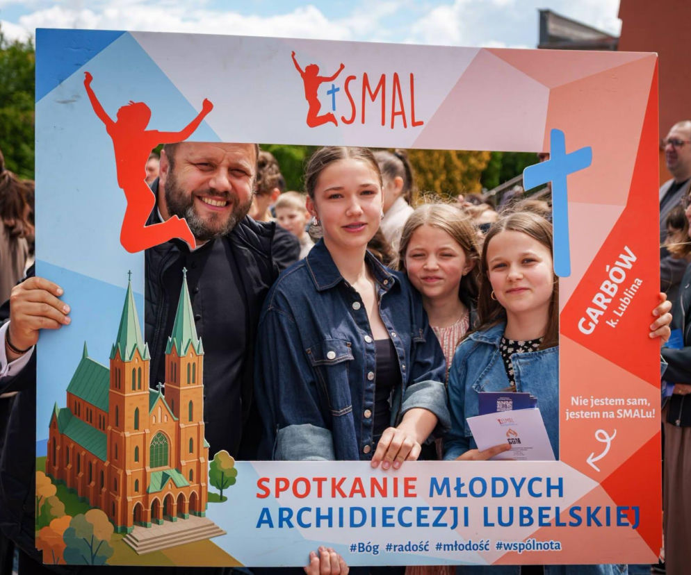 Uśmiechnięty ksiądz z grupą młodzieży w pamiątkowej ramce SMAL. O rekolekcjach w Garbowie przeczytasz na Radioplus.