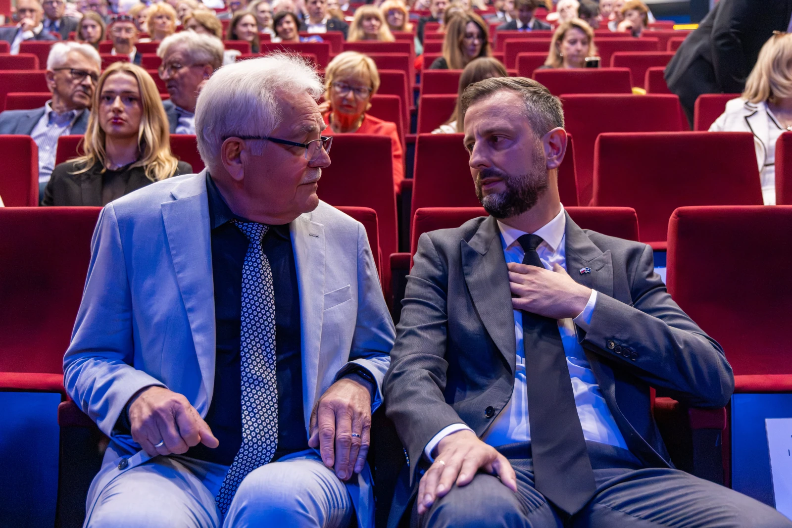 Dwaj mężczyźni w garniturach rozmawiają na tle widowni w sali. Autor: Bogusław Świerzowski
