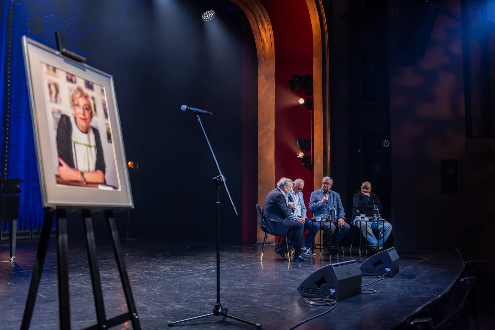 Panel dyskusyjny na scenie z portretem osoby na sztaludze. Autor: Bogusław Świerzowski
