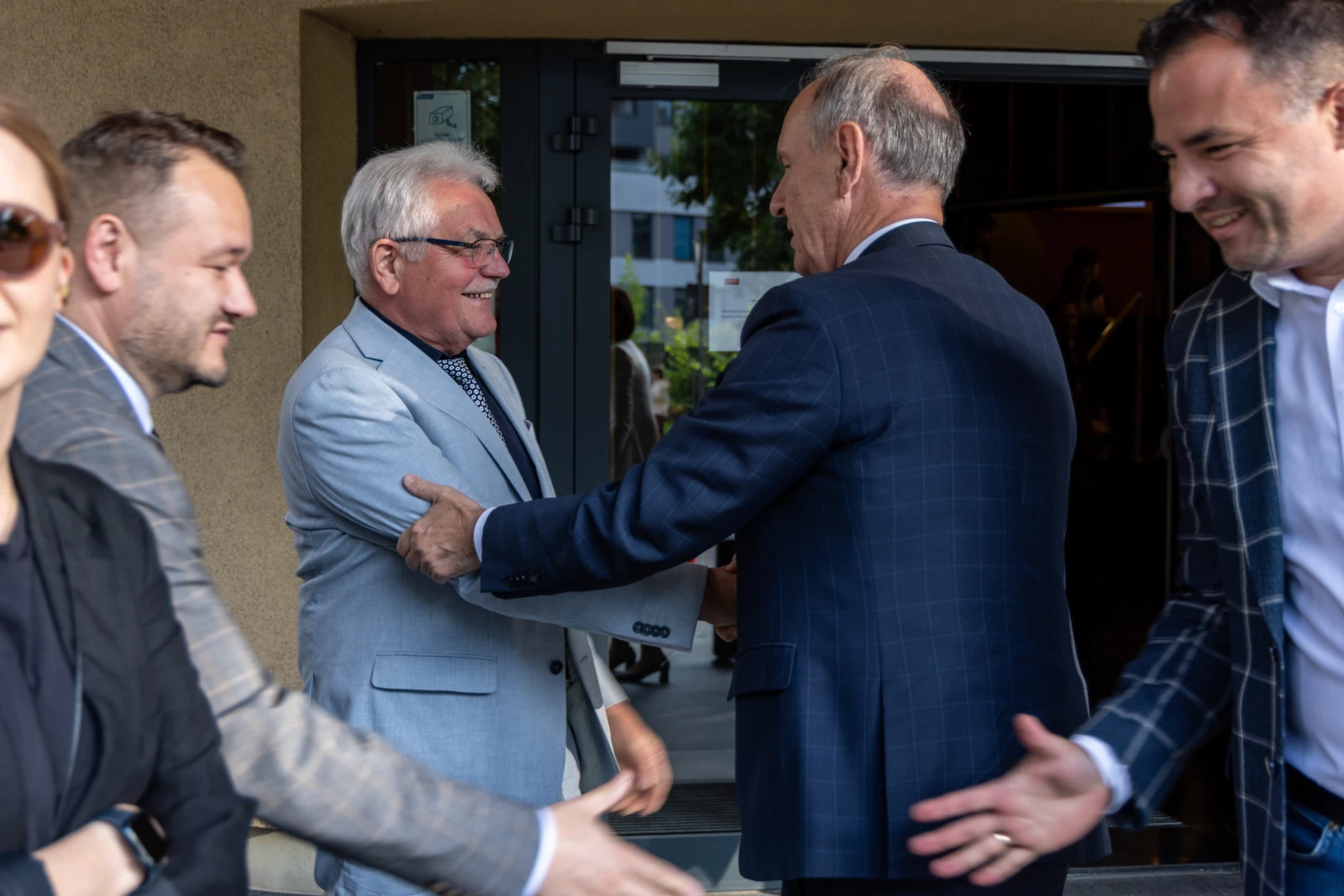 Grupa mężczyzn w garniturach wita się na zewnątrz budynku. Autor: Bogusław Świerzowski