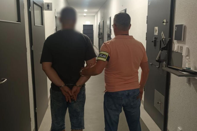 Policjant prowadzi zakutego w kajdanki mężczyznę korytarzem. O zatrzymaniu złodziei z Piły przeczytasz na Eska Poznań.
