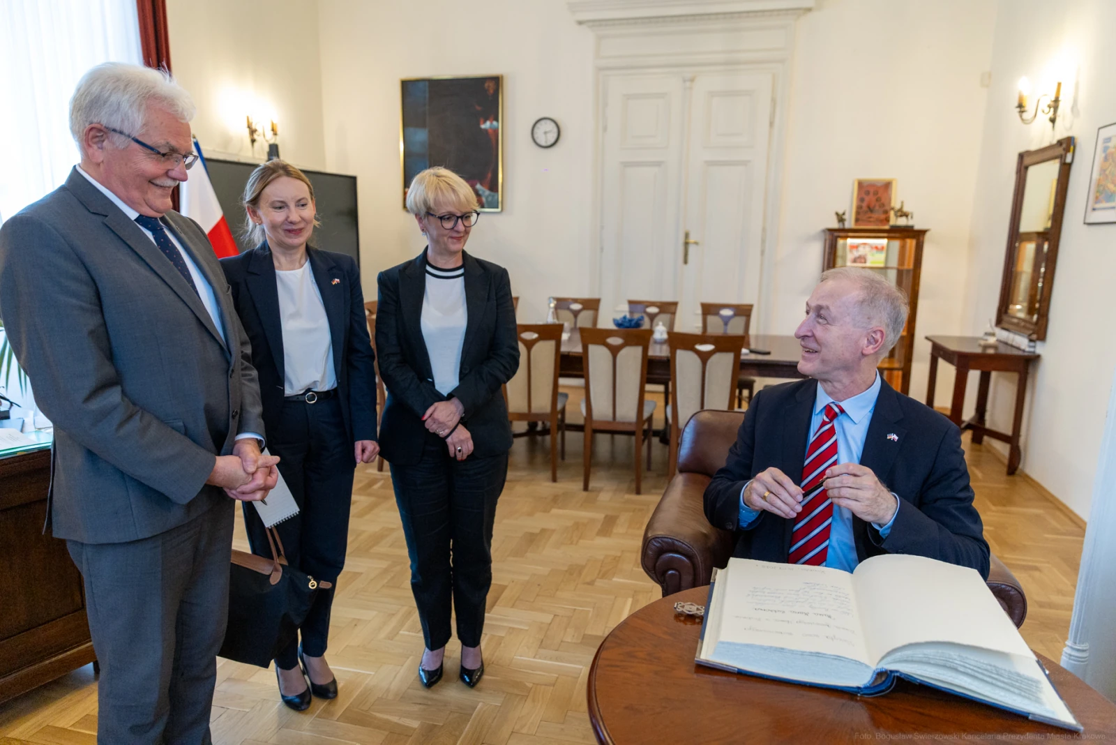 Spotkanie czterech osób w biurze, jedna z nich przy biurku z otwartą księgą. Autor: Bogusław Świerzowski