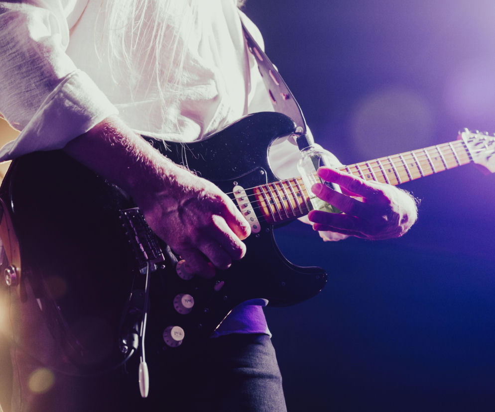 Dłonie muzyka grającego na czarnej gitarze elektrycznej podczas koncertu. O Suwałki Blues Festival przeczytasz na SE Białystok.